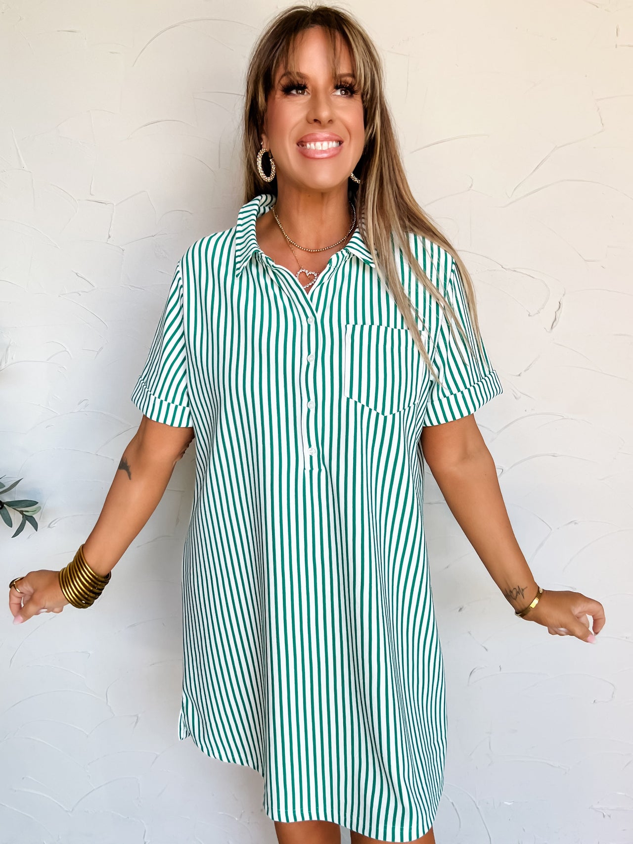 Woman wearing a green and white striped t-shirt dress against a white wall.