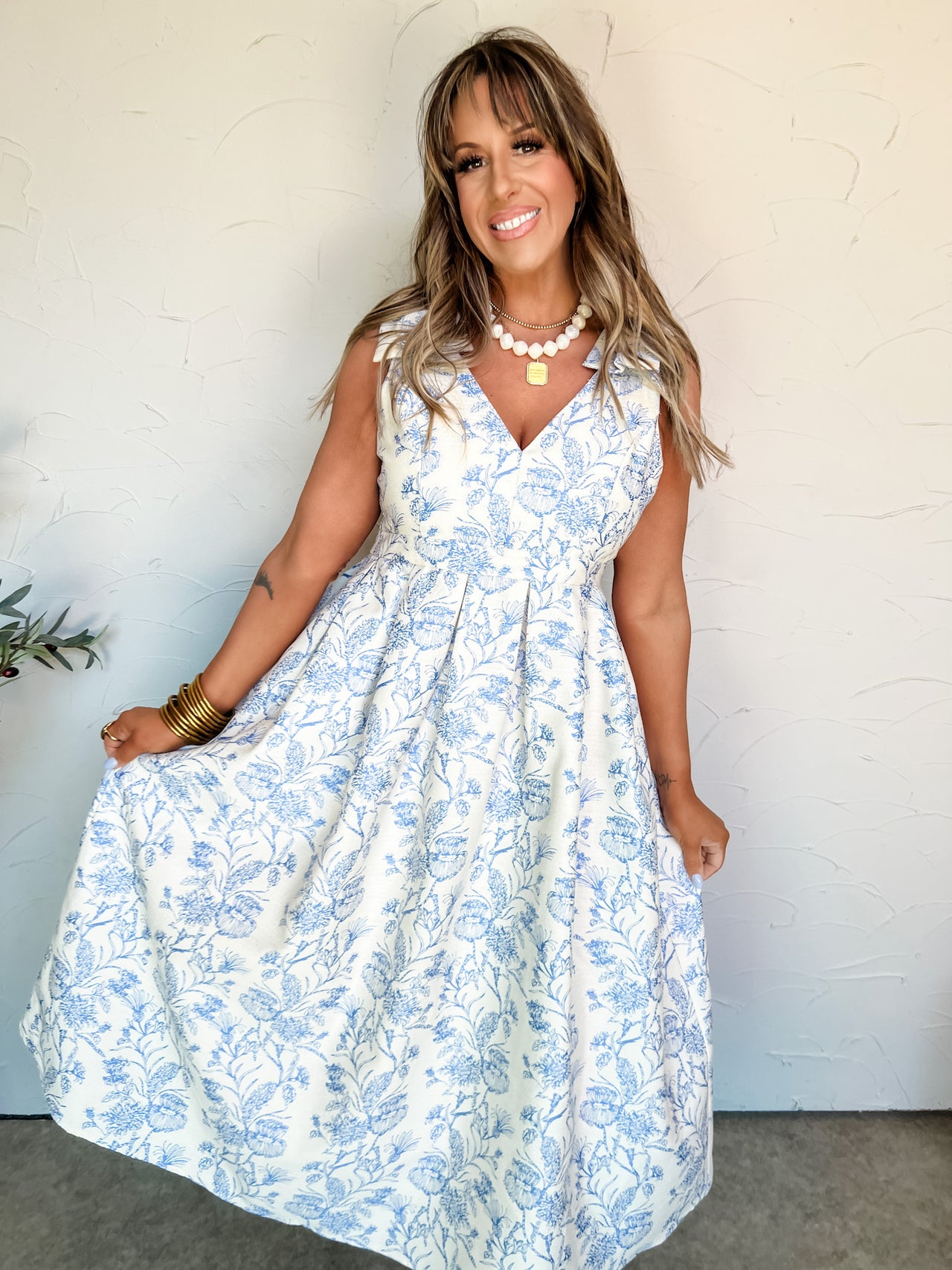 Woman wearing a white dress with blue floral pattern against a white wall.