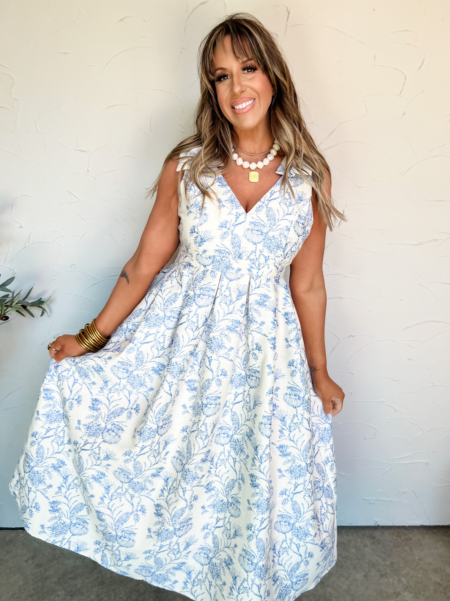 Woman wearing a white dress with blue floral pattern against a white wall.