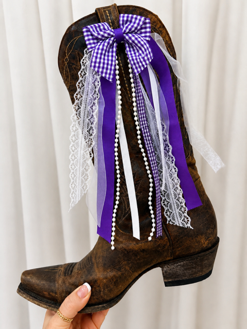 Brown cowboy boot with purple and white decorative ribbons on a white background
