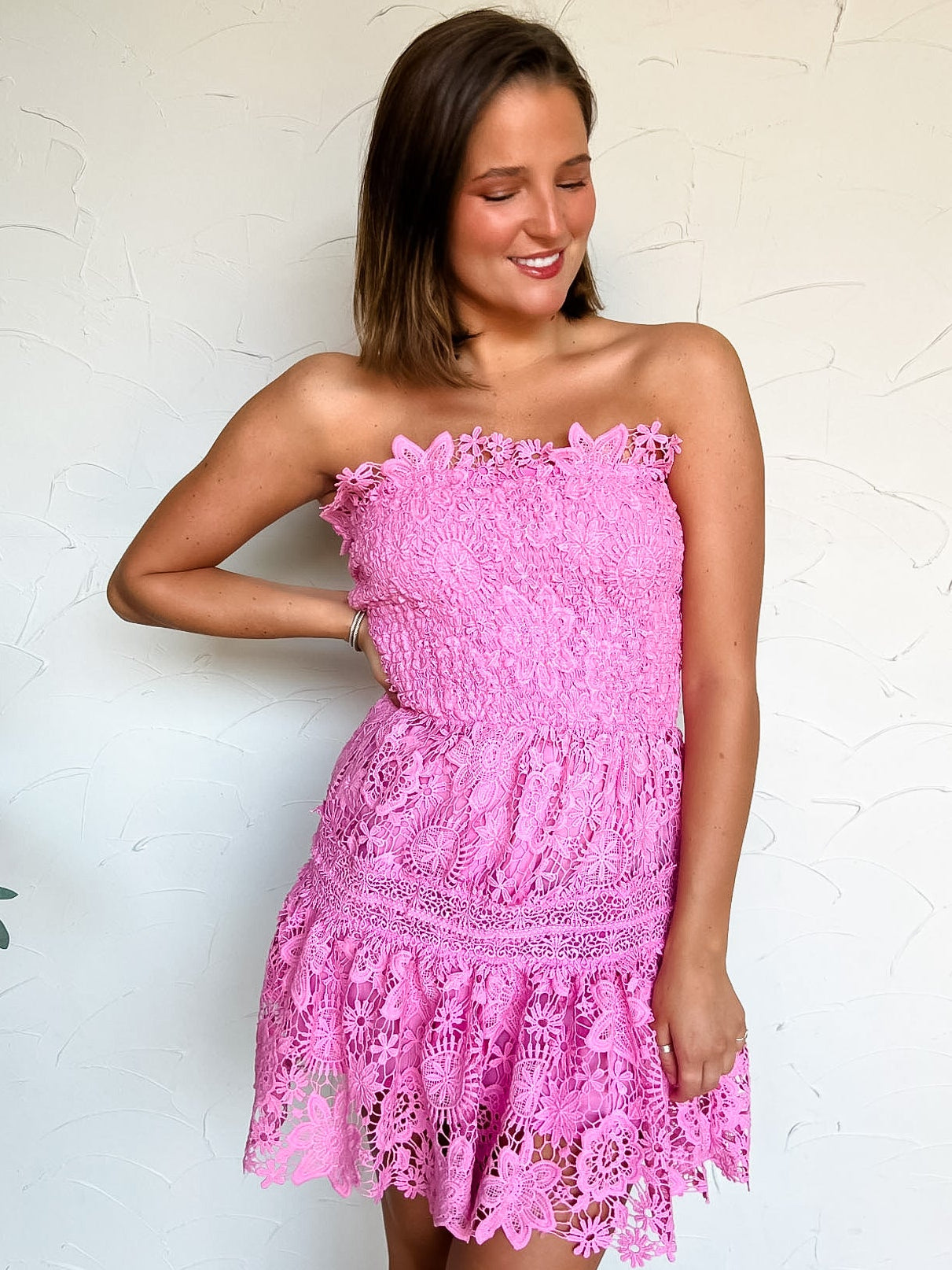 Woman wearing a pink lace strapless dress against a white wall