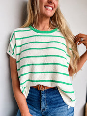 Woman wearing a white and green striped sweater with blue jeans against a plain background