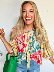 Woman wearing a colorful patterned blouse with a green bag against a white background
