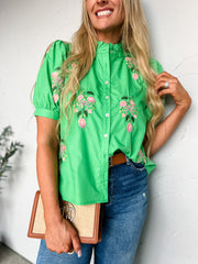 Woman wearing a green floral blouse against a white wall
