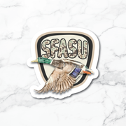 A die-cut sticker featuring a flying mallard duck in front of a shield with the text 'SFASU' in camouflage lettering, shown on a white marble background.