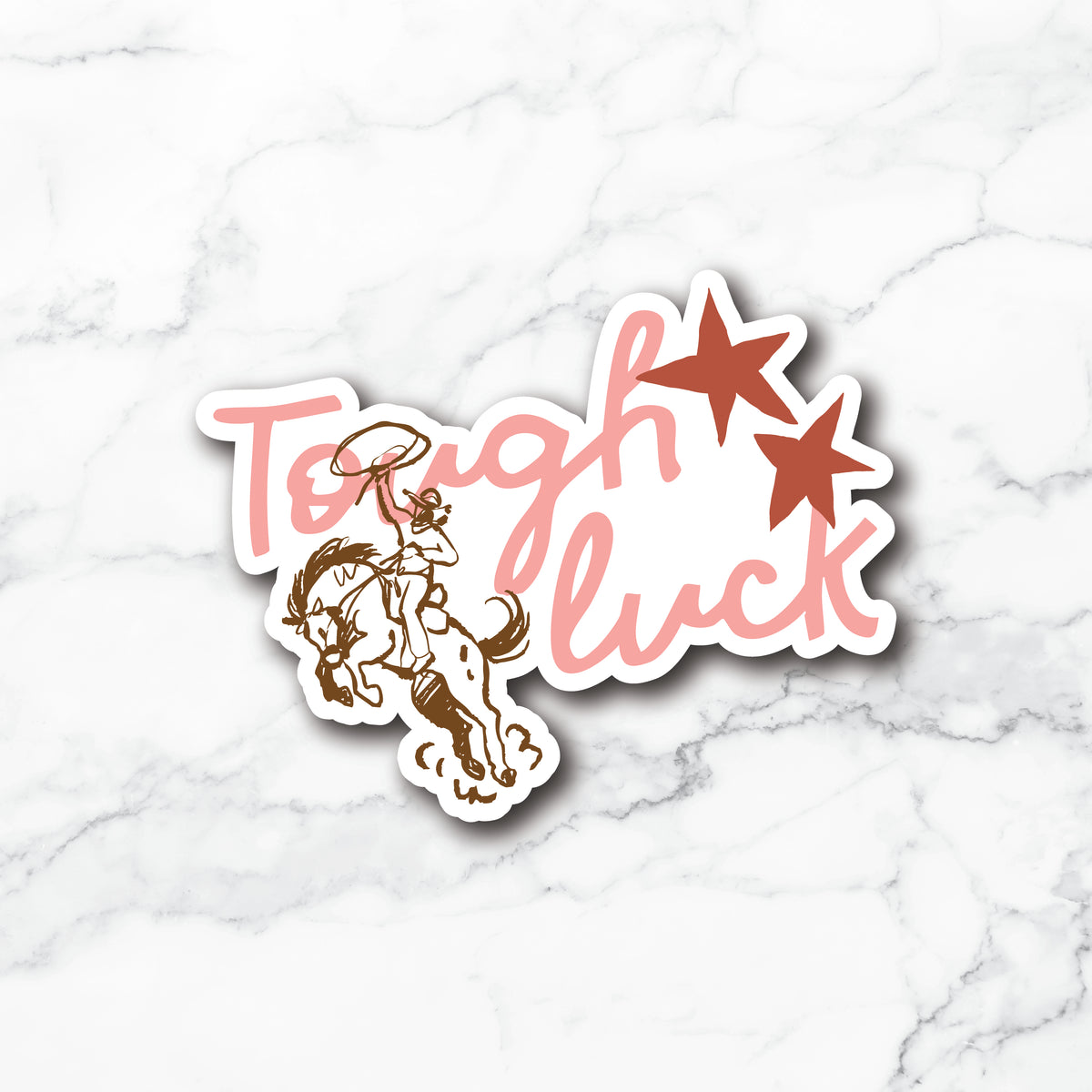 A die-cut vinyl sticker featuring the phrase 'Tough luck' in pink script, accented by two brown stars and a brown cowboy riding a bucking horse. The sticker is presented on a white marble background.